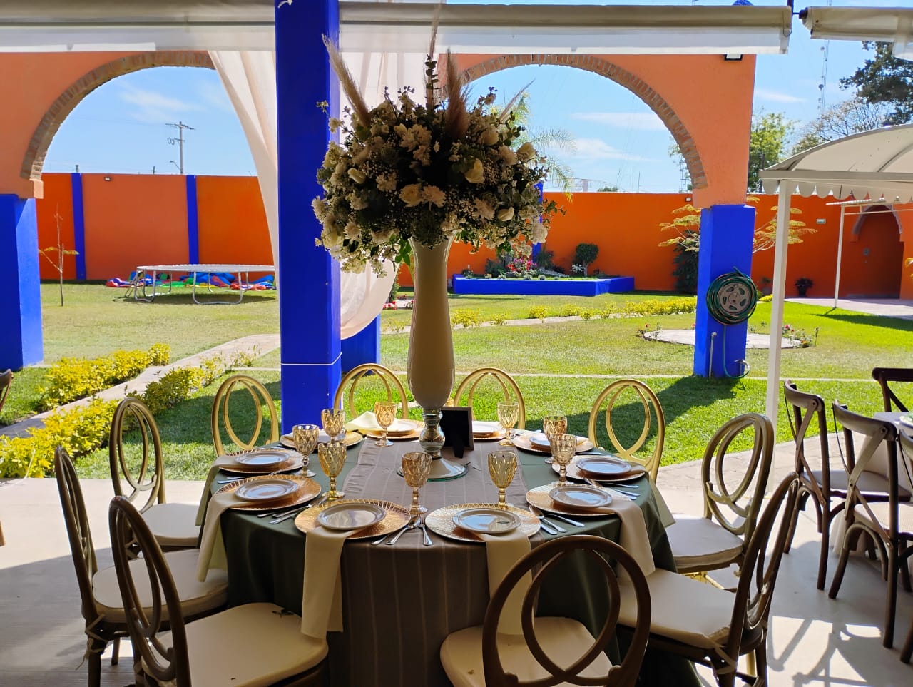 Mesa montada con mantelería, vajilla y arreglo floral, con el jardín al fondo